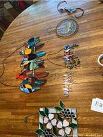 Table view of multiple stained glass decorative items including bird hangings, cat motif, and floral panel.