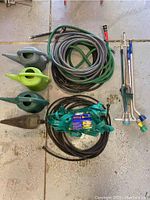 Full view of hoses, watering cans, drip lines, and watering wand implements laid out on floor.