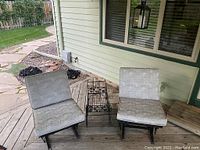Two black wrought iron gliding chairs with grey patterned cushions placed on wooden deck