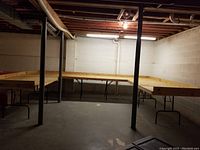 Photo showing four 4 ft by 8 ft tables arranged in a rigid U-shape configuration, connected by bolts and supported by metal folding legs in a basement room