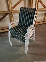 Four white aluminum frame deck chairs stacked together showing green and white striped fabric.