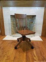 Front view of antique oak office desk chair showing slatted back and contoured seat in front of fireplace.