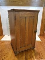Closed view of the antique oak cabinet showing single paneled door and carved wood detail along the top edge.