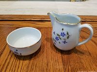 Photo showing Apilco porcelain creamer and sugar bowl placed on a wooden surface, highlighting floral pattern and gold rims.