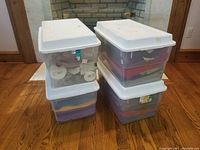 Four stacked plastic storage bins with white lids containing fabric and trims