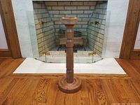 Full view of the hand-turned wooden candle stand against a fireplace background, showing overall height, shape, and base width.