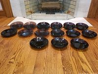 Overall lot showing 7 Moroccan Swirl amethyst plates and 8 matching bowls arranged on wooden floor in front of fireplace
