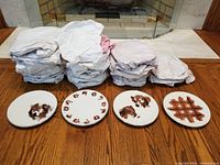 Overall view of 25 wrapped plates with four plates displayed showing different dog portrait patterns and one plaid design, all with silver tone rims.