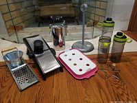 All kitchen items shown together: OXO mandolin, spaetzle maker, metal pitcher, gelatin mold, paper towel holder, pancake form, and two Rubbermaid water bottles