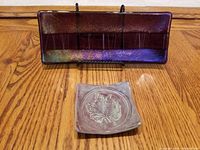 Both dishes displayed together on wooden table: rectangular dichroic glass dish with colorful reflective surface and small square ceramic dish with embossed leaf.