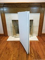 Side view of white wooden sandwich board with two wide flat panels joined with hinges, standing upright near fireplace.