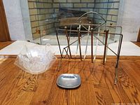 Photo showing the wire magazine stand, Wilton pewter ashtray, and the stacked acrylic handkerchief bowls arranged on a wooden surface in front of a fireplace.