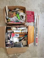 Top view of two boxes filled with assorted tools, hardware items, spray cans, and small packaged components.