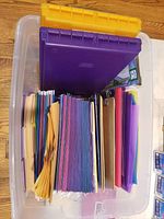 Photo of clear plastic container filled with colorful paper tab folders, hanging folders and two pocket folders in yellow, purple, blue and pink.