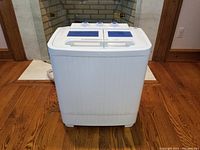 Front view of white portable washing machine on wood flooring.