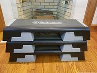 Stack of three black and gray Reebok step exercise platforms showing side profile and rubber feet on top surfaces.