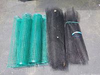 Top view of 7 rolls of deer fencing arranged in two groups – 4 green rolls bundled and 3 black rolls bundled on asphalt surface