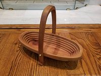 Full view of the wooden oval basket bowl with handle in upright position, showing the spiral cut layers and wood grain.