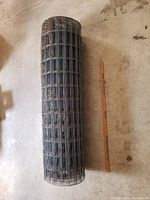 Top view of the rolled welded wire fencing spool beside a wooden yardstick for scale showing height and overall condition.