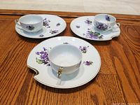 Full view of the three tea cups each paired with a matching snack plate, showing violet floral patterns and gold rims