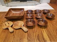 Full set of wooden salad bowls and serving bowl with salad tongs arranged on wood floor
