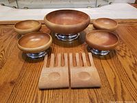Set of 4 medium wooden salad bowls and 1 larger wooden salad bowl, each with chrome bases, arranged on wooden surface.