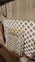 White lattice panel 8'x4' leaning against wall with three baby/pet gates stacked leaning in front of it.