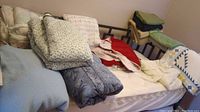 Photo of multiple blankets, quilts, comforters, and bedspreads stacked on a bed and chair showing different colors, textures, and patterns.
