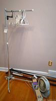 Photo of collapsible metal clothes rack with assorted plastic and metal hangers, curtain rods stacked horizontally on floor, and Honeywell table fan in front.