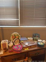 Wide view of all the decorative boxes, ceramic clock, and glass chicken on a wooden dresser under window blinds.