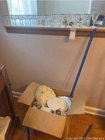 Photo showing the box with various Johann Haviland dishes inside and a row of 23 metallic-edged glasses displayed on a ledge above.