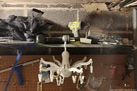 Top shelf with Ryobi drill, Brad nailer, metal pipes, hardware, and white multi-arm clothes hanger with clips.