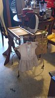Photo showing the metal ironing board with Black and Decker electric iron placed on it, wooden washboard leaning against the board, and a metal wire record stand nearby. The setting is a basement with various other furniture visible in background.