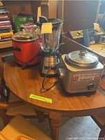 Photo showing all three appliances on a wooden table: Cuisinart rice cooker in front, Hamilton Beach blender behind it, and red Crock-Pot slow cooker to the left.