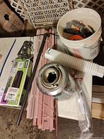 Full view of lot showing bundled dusty pink window blinds, metal staple guns, InSinkErator garbage disposer with flexible hose, white bucket filled with hand tools and hardware including doorknob.