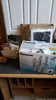 Photo of Panasonic KXTGE275 phone system box, various office supplies and miscellaneous items on desk