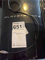 Top view showing the PlayStation 3 logo on the console's glossy black surface with visible scratches and attached power/USB cable.