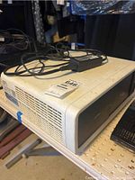 Overall view of the off-white Sanyo projector with power adapter cable on top, showing side vent area and surface detail.