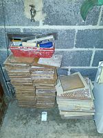 Two stacks of used floor tiles in beige and brown with grout tools in a red tray on top.