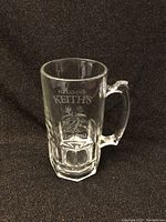 Front view of the thick glass beer mug with Alexander Keith's logo etched on it showing lion and stag imagery.