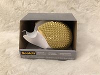 Front view of the sealed tape dispenser in its box showing the hedgehog design and Scotch branding.