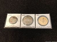 Four coins shown in cardboard holders with handwritten event names and years on the front side.