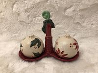 Photo showing front angle of the holiday-themed ceramic salt and pepper shakers on the red holder with green leaf detail.