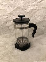 Front and side view of IKEA coffee press made of glass with a black handle and lid, plus stainless steel plunger.