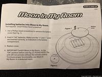 Instruction manual page for installing batteries into the Moon In My Room nightlight, showing battery compartment details and cover removal