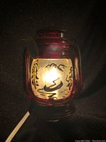 Front view of electric night light lantern illuminated showing canoe and mountain silhouette design on glass panel.