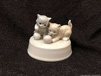 Front side view showing two kittens playing with a ball of yarn crouched on circular base