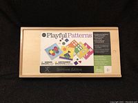 Wooden box with cover label showing colorful shapes and pattern cards, branded MindWare Playful Patterns Heirloom Edition