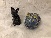 Front view of black lacquerware cat figurine and blue ceramic curled cat box on fur background.