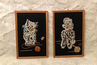 Pair of vintage embroidered wall hangings showing cat and dog images on black fabric in simple wooden frames